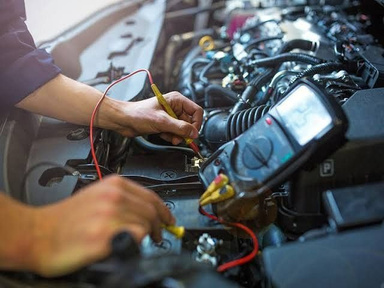 Technician checking a car electrical system with a multimeter